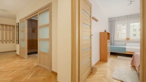 A room with a herringbone floor, a sliding wooden door with frosted glass panels, a bed with a blue bedspread, and a window with a view of buildings. - Spacious Apartment | 2 Bedrooms and Balcony close to the Center (Warszawa)