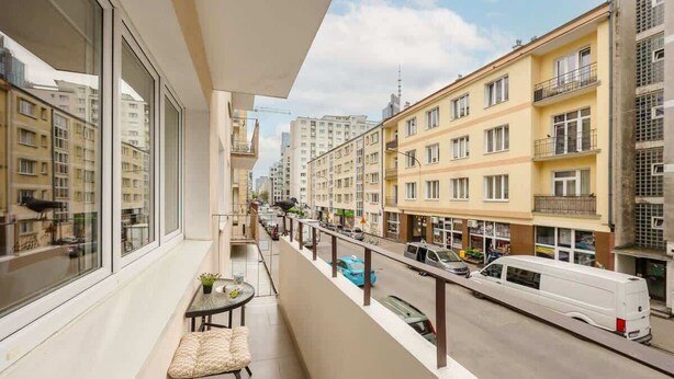 A balcony with a view of a city street, a table with a chair, and a small plant. - Spacious Apartment | 2 Bedrooms and Balcony close to the Center (Warszawa)