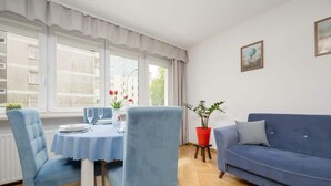 A dining area with a table set for two, a blue sofa, and a window with curtains. - Spacious Apartment | 2 Bedrooms and Balcony close to the Center (Warszawa)