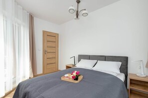Une chambre à coucher bien rangée, avec un lit, des tables de chevet, une commode, une armoire en bois et une fenêtre avec des rideaux.