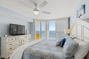 Een slaapkamer met een bed, een televisie, een dressoir en een balkon met uitzicht op de oceaan.