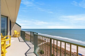 Een balkon met gele Adirondack-stoelen met uitzicht op een strand.