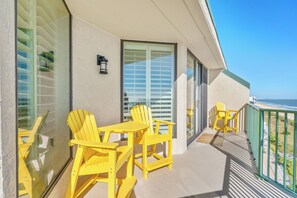 A balcony with yellow chairs and a table, a large window with blinds, and a view of the ocean. - Recently updated oceanfront unit, wonderful views + Free Attraction Tickets! (North Myrtle Beach)
