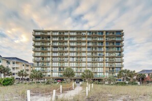 A multi-story hotel with balconies, a sandy pathway, and surrounding vegetation. - Recently updated oceanfront unit, wonderful views + Free Attraction Tickets! (North Myrtle Beach)