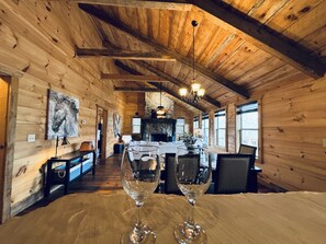 Ein Holzblockhaus-Interieur mit Essbereich, inklusive Tisch, zwei Weingläsern, einem Steinkamin und Holzwänden.