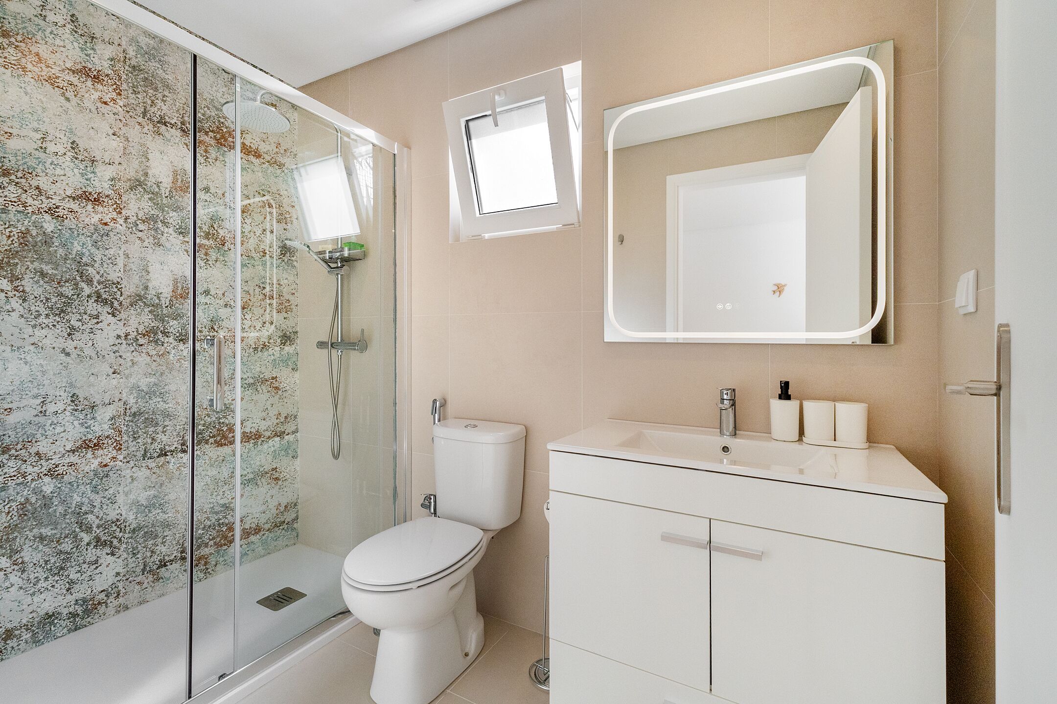 A bathroom with a glass-enclosed shower, a toilet, a sink with a mirror, and a wall-mounted light fixture.