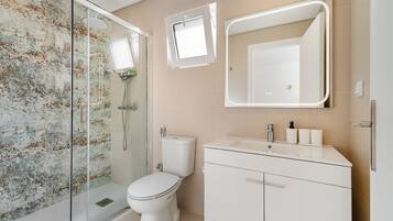 A bathroom with a glass-enclosed shower, a toilet, a sink with a mirror, and a wall-mounted light fixture.