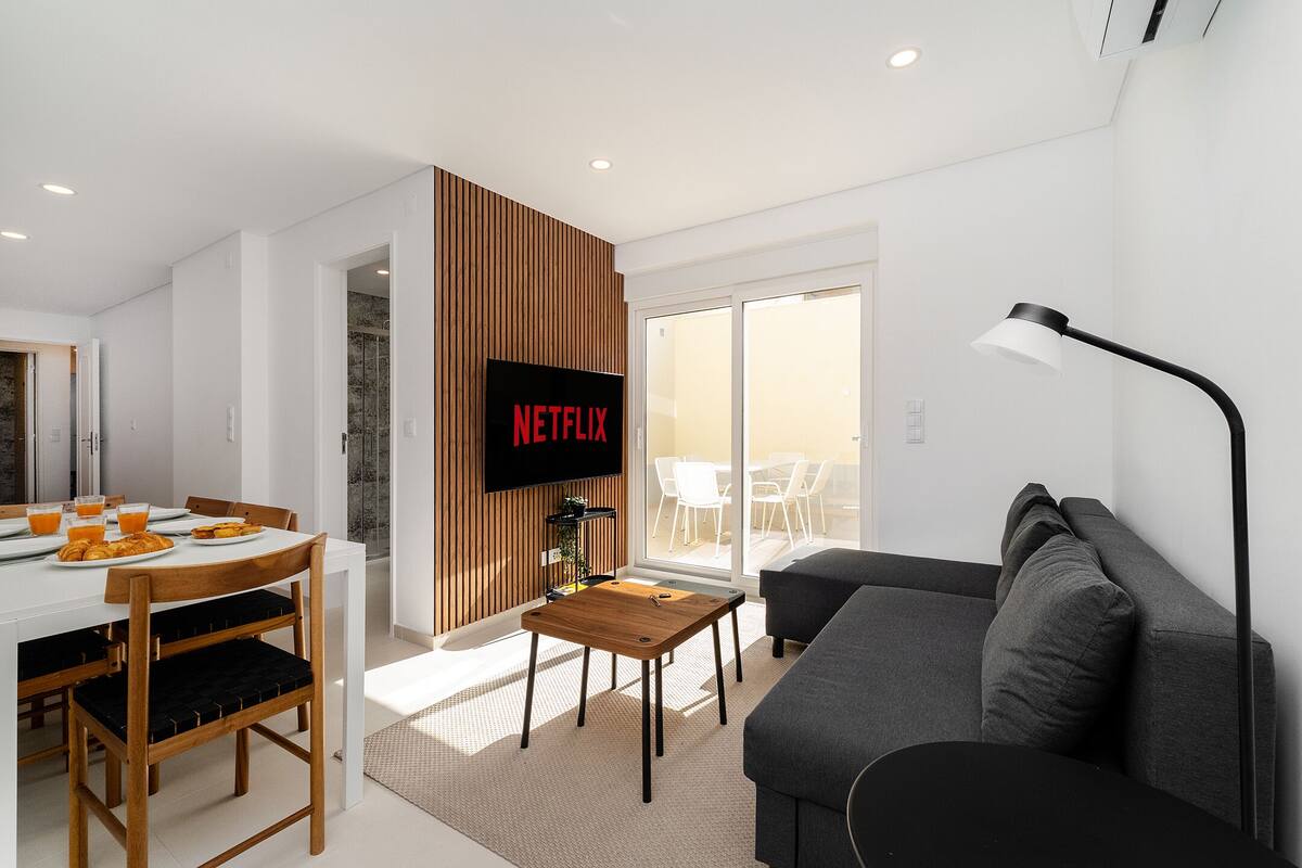 Una sala de estar moderna con un sofá, una mesa de centro y un televisor montado en una pared de madera que muestra