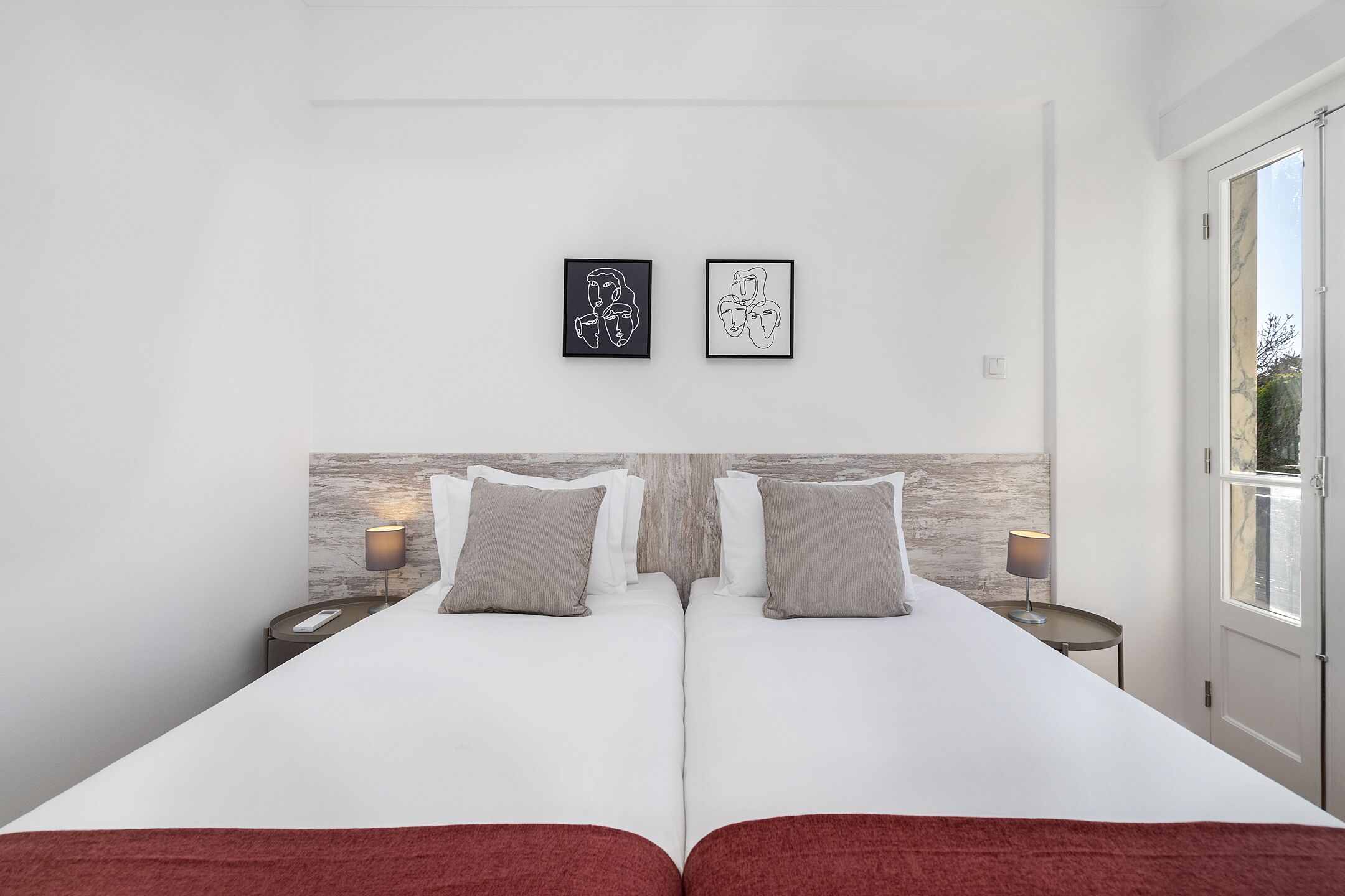 Una cama doble con ropa de cama blanca y dos almohadas, un cabecero de madera, dos mesitas de noche con lámparas y dos obras de arte enmarcadas en la pared.