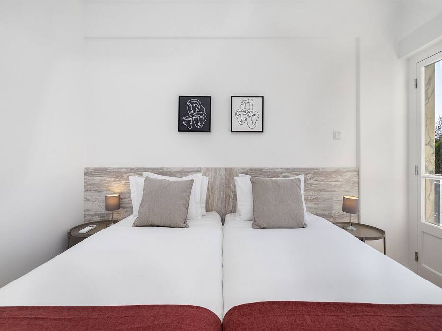 Una cama doble con ropa de cama blanca y dos almohadas, un cabecero de madera, dos mesitas de noche con lámparas y dos obras de arte enmarcadas en la pared.
