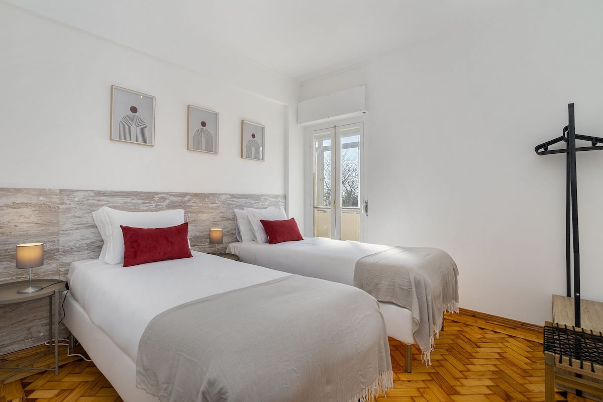 Habitación de hotel con dos camas, piso de madera, ventana y perchero.