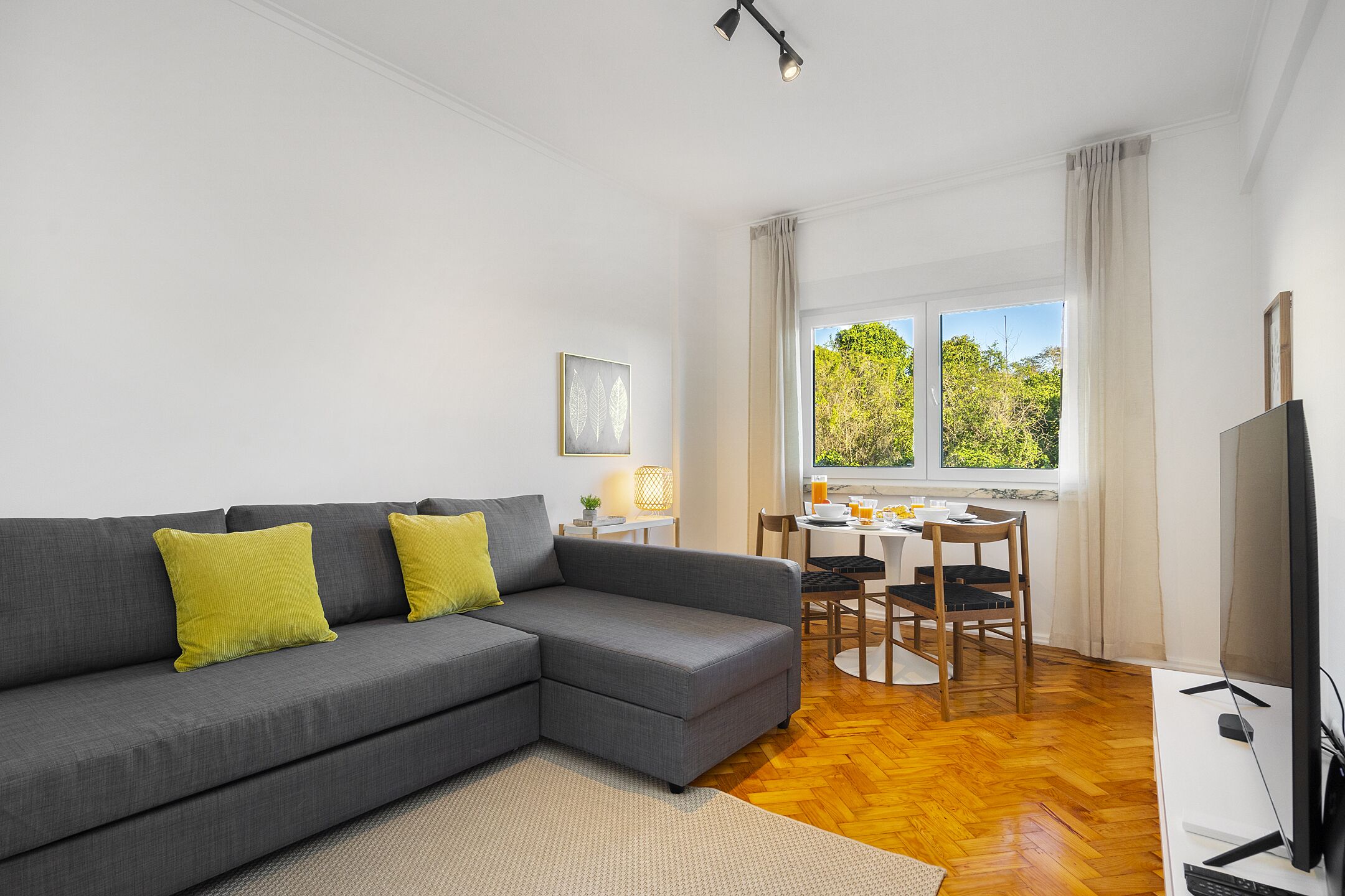 A modern living room with a grey sectional sofa, a dining area with a table and chairs, and a TV on a stand.