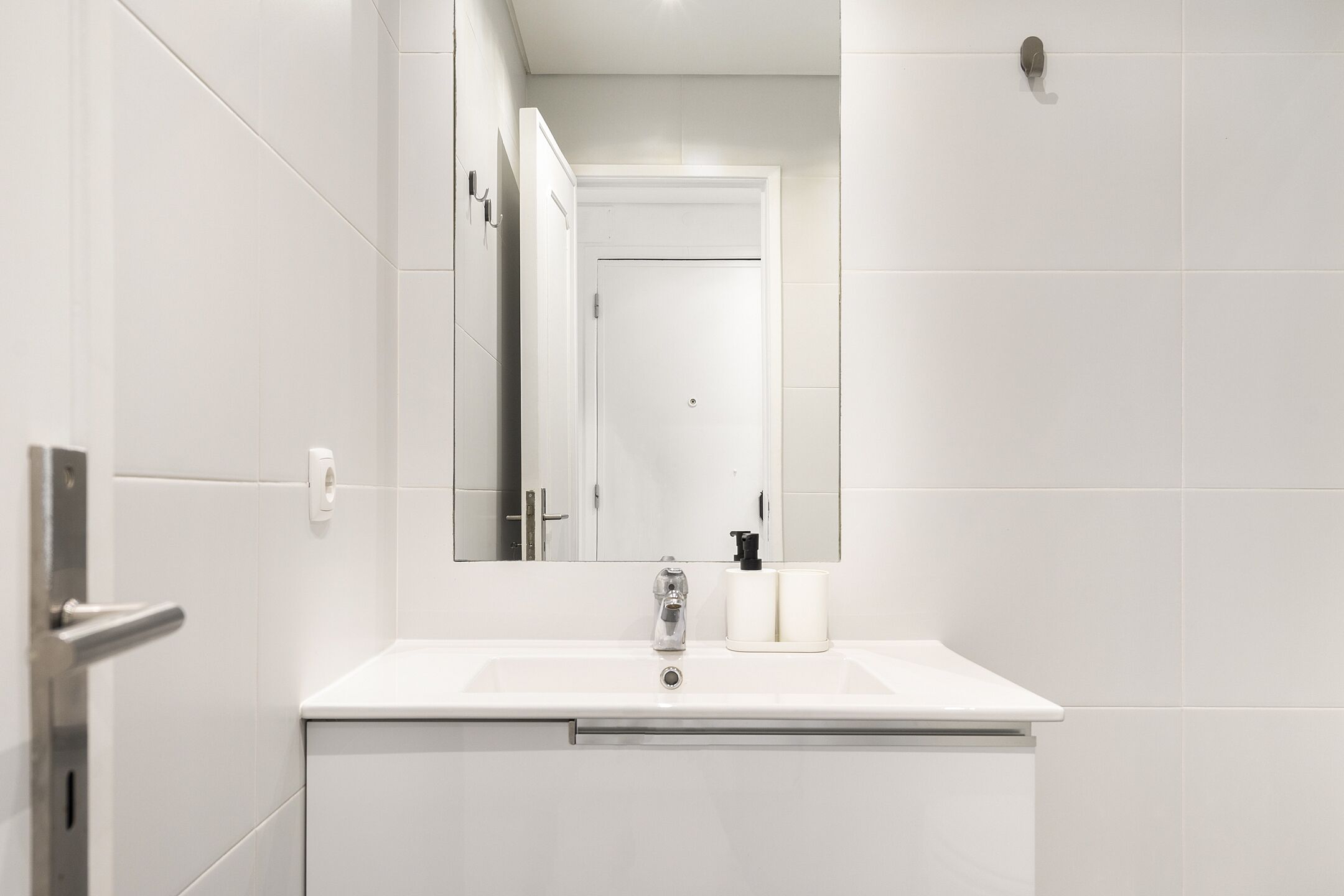 Un baño moderno con azulejos blancos, un lavabo con grifo, un espejo y un inodoro.