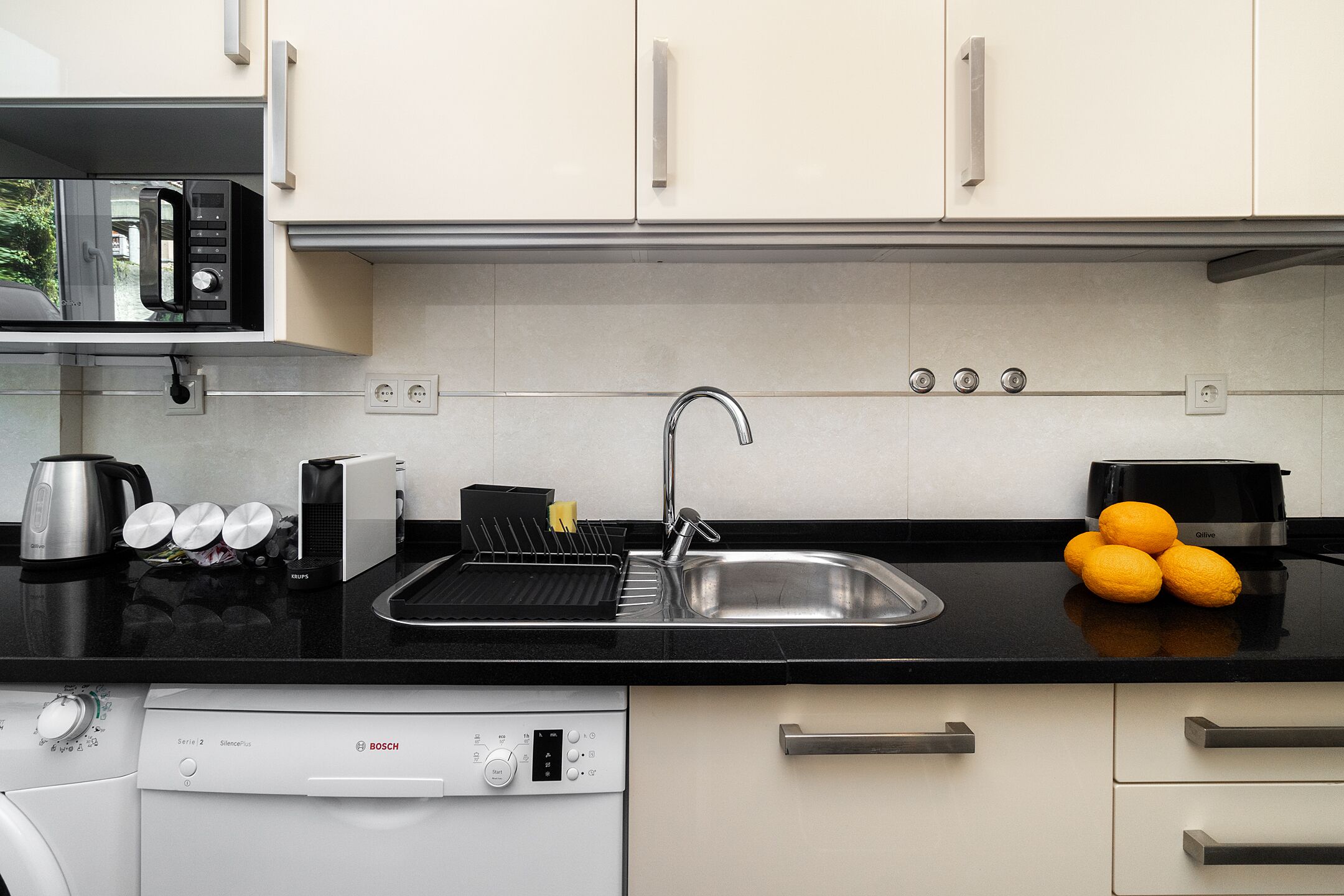 Una cocina moderna con encimera negra, pileta de acero inoxidable y armarios blancos.