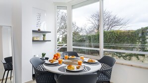 A breakfast table with croissants, orange juice, and a view of trees through large windows. - Peaceful Algés Family Home (Oeiras)