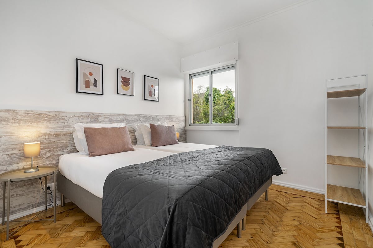 Un dormitorio con cama, mesita de noche, lámpara y ventana con vista a la vegetación.