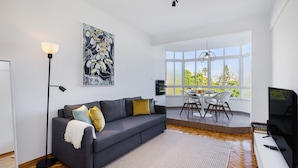 A modern living room with a grey sofa, a floor lamp, and a dining area with a table and chairs. - Peaceful Algés Family Home (Oeiras)