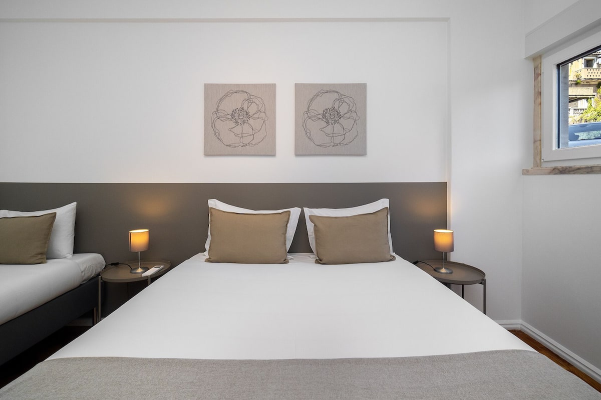Una habitación de hotel moderna con una cama grande, dos mesitas de noche con lámparas, un cabecero y dos obras de arte colgadas en la pared.