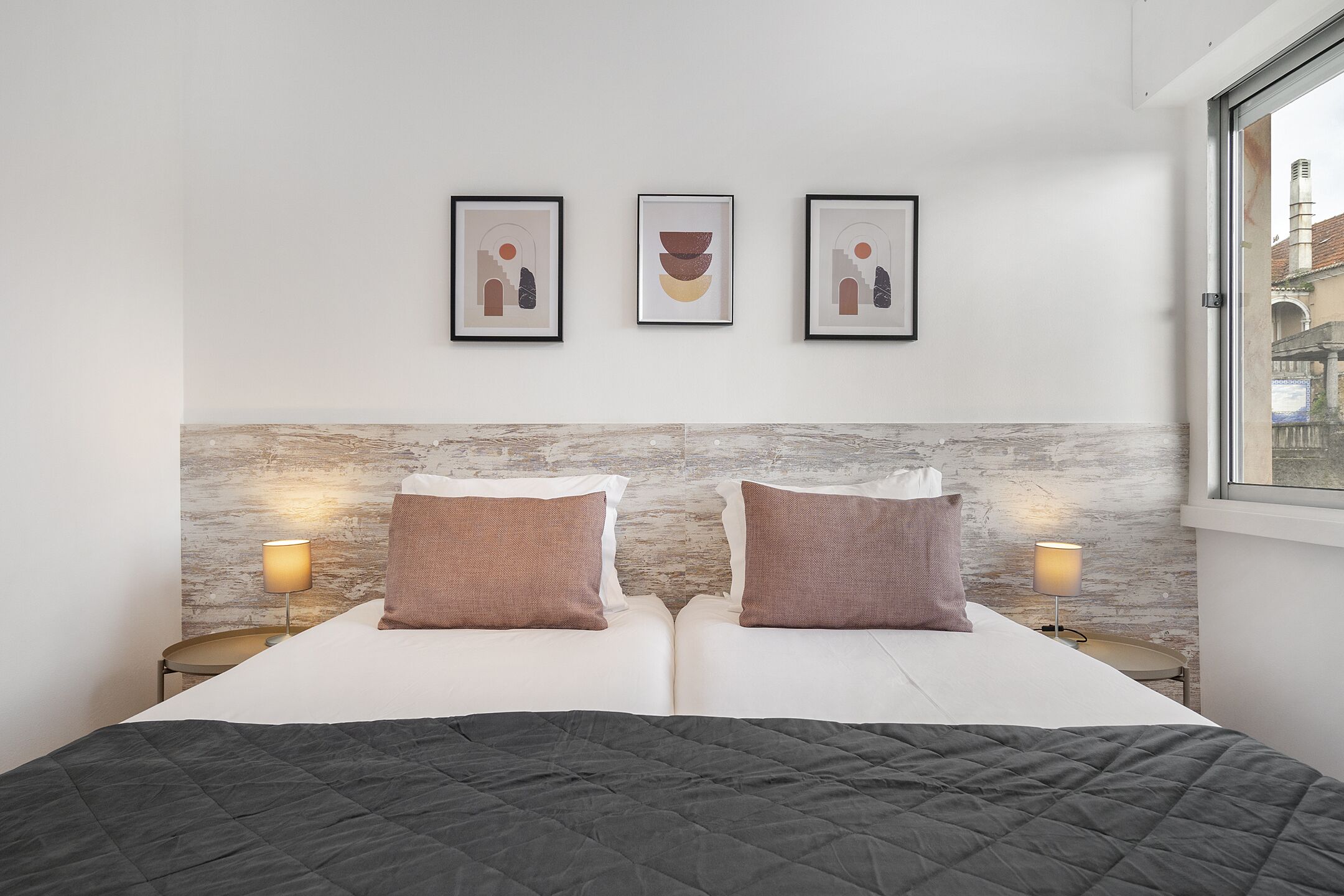 A double bed with a dark quilt, two bedside lamps, and three framed artworks on the wall.