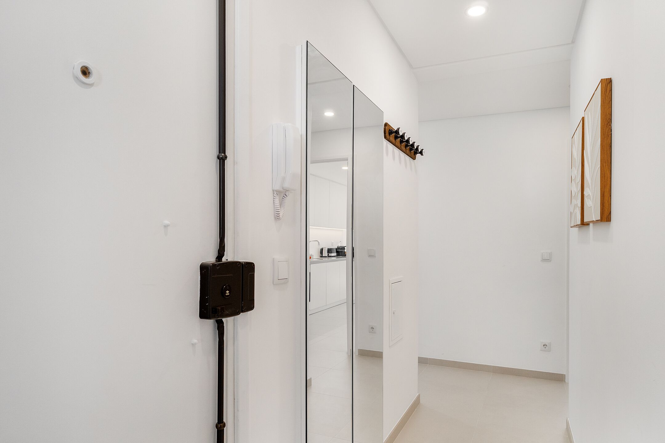 A hallway with a mirrored wall, a coat rack, and a door leading to a bathroom.