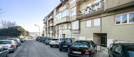 A row of parked cars in front of a multi-story building with balconies.