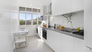 A modern kitchen with white cabinets, a stainless steel sink, and a window providing natural light. - Peaceful Algés Family Home (Oeiras)