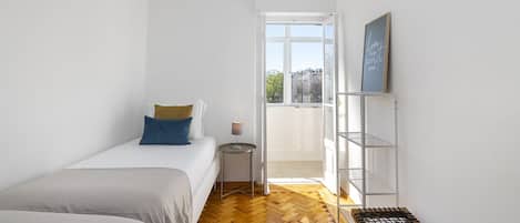 Ein Schlafzimmer mit zwei Betten, einem kleinen Nachttisch mit Lampe, einer Holzbank, einer weißen Wand und einem großen Fenster mit Blick.