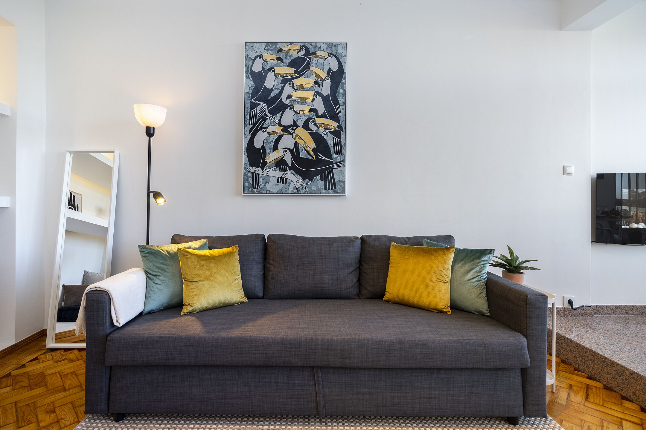 A modern living room with a grey sofa, yellow and green cushions, a floor lamp, and a large abstract painting on the wall.