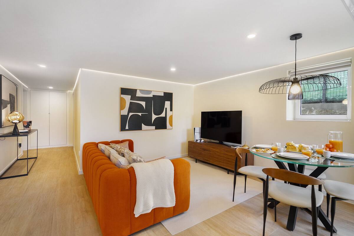 A modern living room with a sofa, a dining table with chairs, a TV, and artwork on the wall.