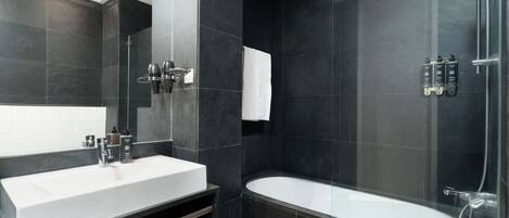 A modern bathroom with a large white sink, a glass-enclosed shower, and dark tiled walls.