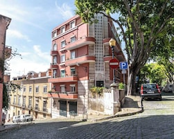 Um edifício com vários andares e varandas, uma rua de paralelepípedos e um carro estacionado.
