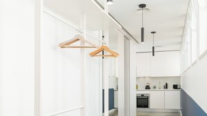 Un pasillo moderno y minimalista con estanterías blancas, una cesta tejida y una zona de cocina al fondo.
