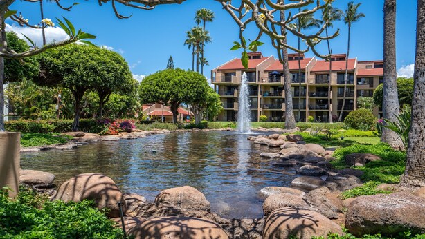 A resort with a pond, palm trees, and a building with balconies.