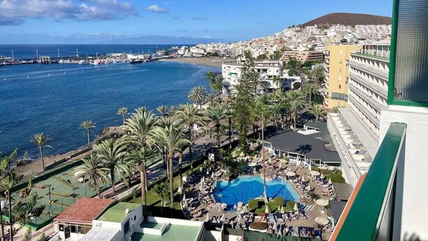 Et kystresort med swimmingpool, palmer og udsigt til havet og bybilledet.