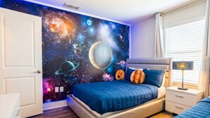A bedroom with a bed, a nightstand, a wall mural of space, and a window with blinds. - Storey Lake 5BR w/ Pool | Near Disney (Kissimmee)