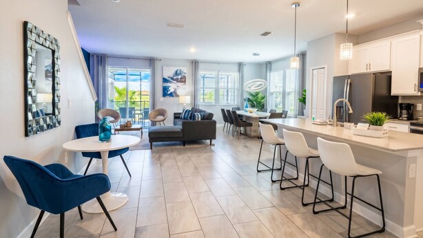 A modern kitchen with a central island, dining area with chairs, and a living room with a sofa and chairs. - Storey Lake 5BR w/ Pool | Near Disney (Kissimmee)