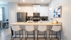 A modern kitchen with a central island, bar stools, stainless steel appliances, and pendant lighting. - Storey Lake 5BR w/ Pool | Near Disney (Kissimmee)