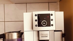Una cafetera con pantalla digital y una tetera sobre una encimera de cocina.