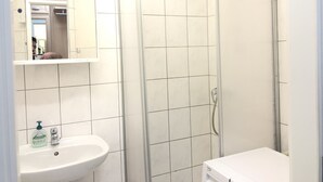 Un baño con lavamanos blanco, espejo y cabina de ducha.