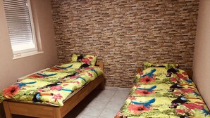Una habitación con dos camas de madera, ropa de cama con motivos florales, una pared de ladrillo y una ventana con persianas.