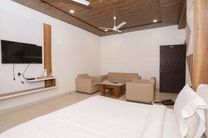 A modern hotel room with a large bed, a sofa, a coffee table, a TV mounted on the wall, and a wooden door.