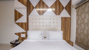 Een net opgemaakt bed met hoofdbord, nachtkastje met lamp, en een behang met patroon.