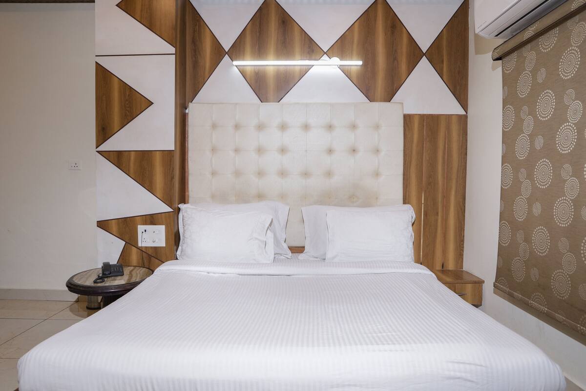 A neatly made bed with a headboard, a bedside table with a lamp, and a patterned wall.