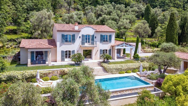A two-story house with a swimming pool, surrounded by lush greenery and trees.