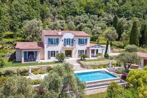 Une maison à deux étages avec une piscine, entourée d’une végétation luxuriante et d’arbres.