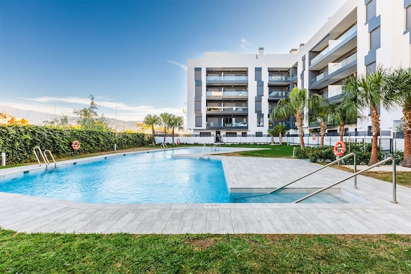 Un edificio moderno con piscina, palmeras y cielo despejado.