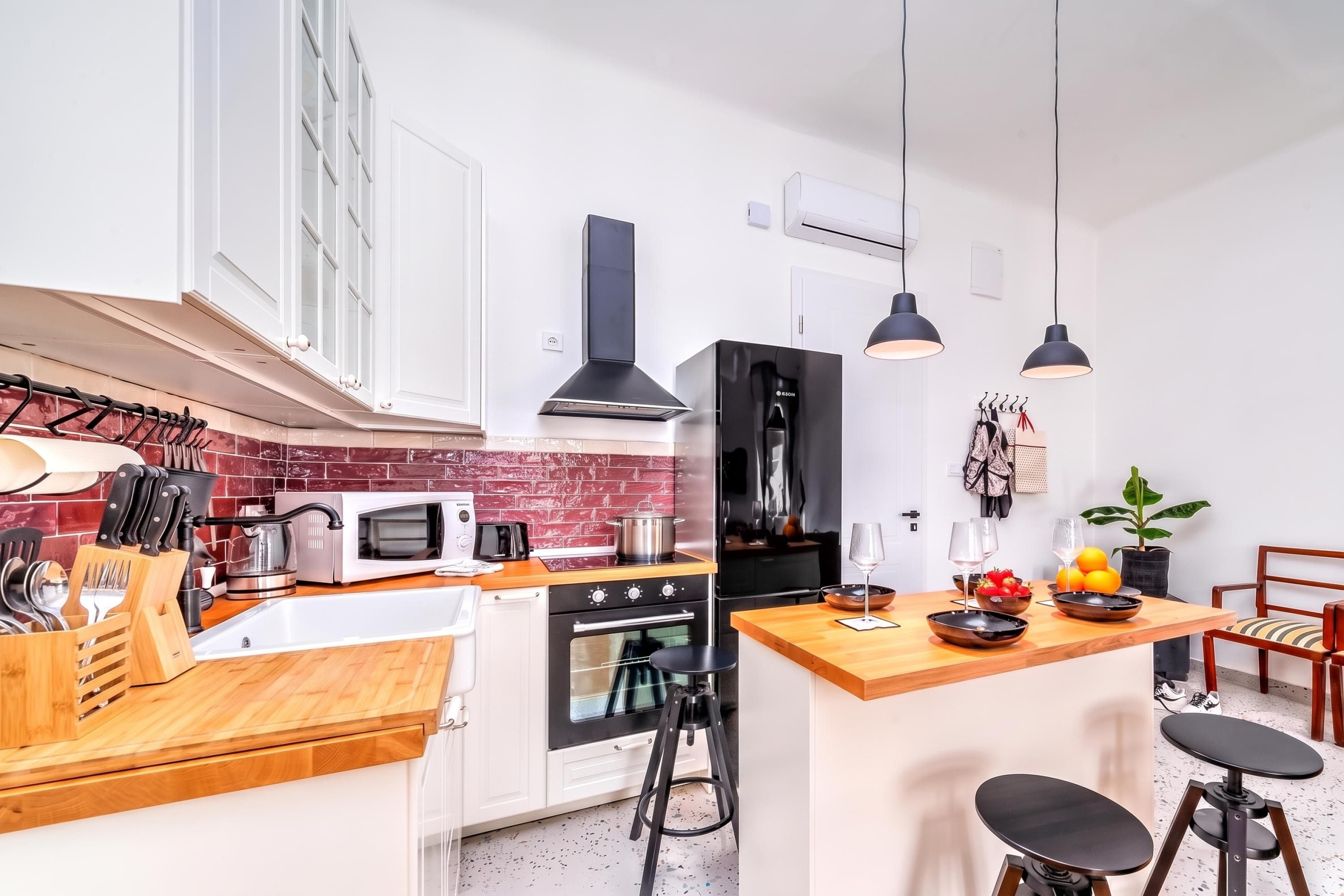 A modern kitchen with white cabinets, a red brick backsplash, and a central island with stools.