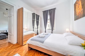 A modern hotel room with a large bed, a mirror, a wardrobe, and a view of the city.