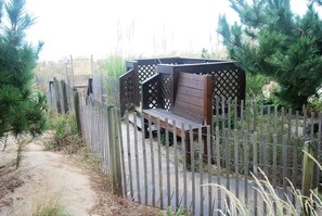 Un banco de madera con respaldo de celosía, rodeado por una valla de madera y vegetación.