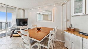 A modern dining area with a wooden table, white chairs, a television, and a view of the outdoors.